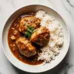 Bowl of smothered chicken and rice garnished with fresh parsley on a marble background