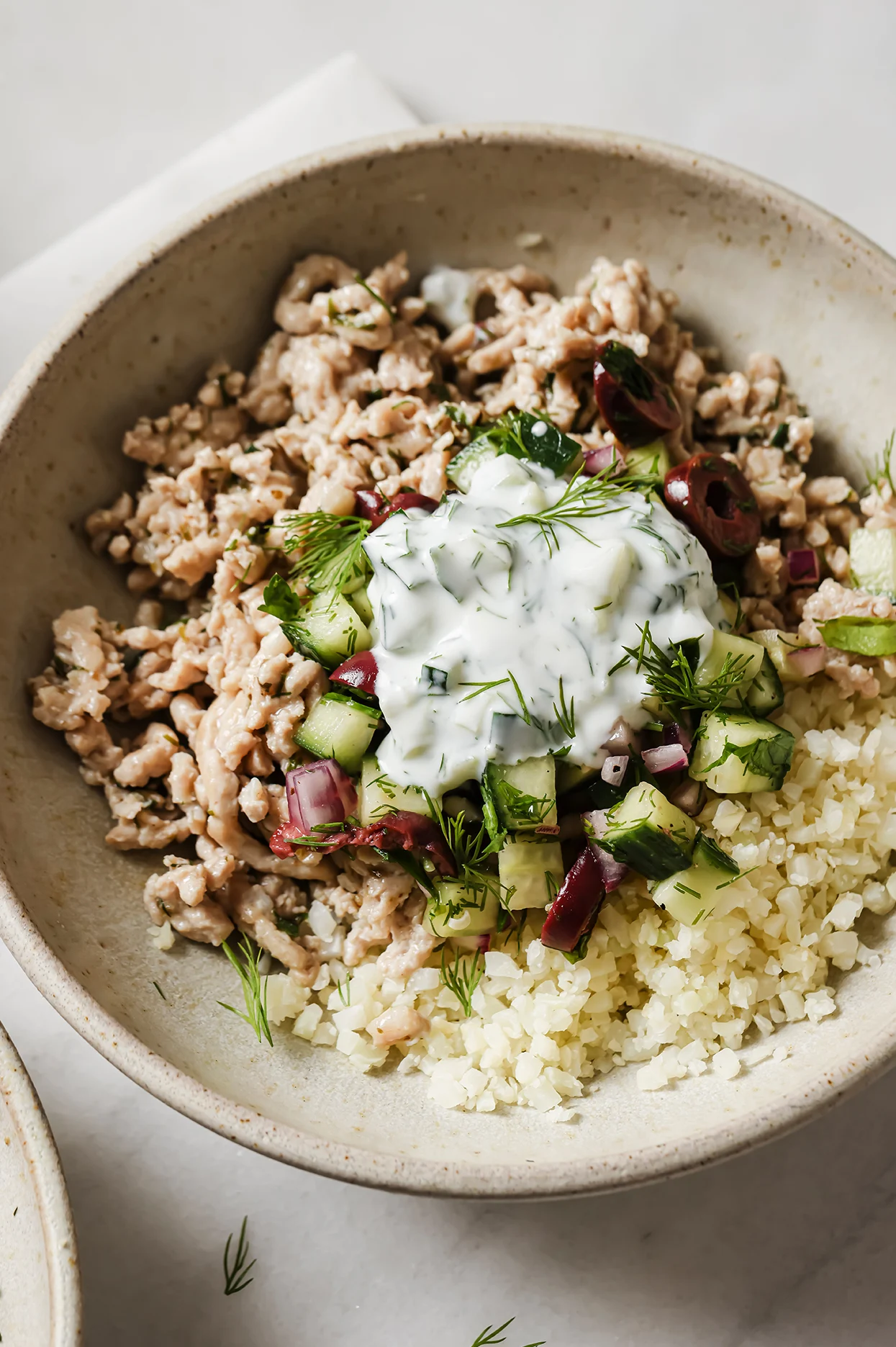 healthy ground chicken bowl with cucumber salad, tzatziki, and cauliflower rice