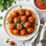 Plate of spaghetti topped with baked chicken meatballs in marinara sauce, garnished with fresh parsley.