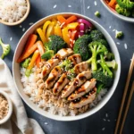 Rice bowl with chicken, broccoli, carrots, bell peppers, and red onion, drizzled with dark sauce and sprinkled with sesame seeds.