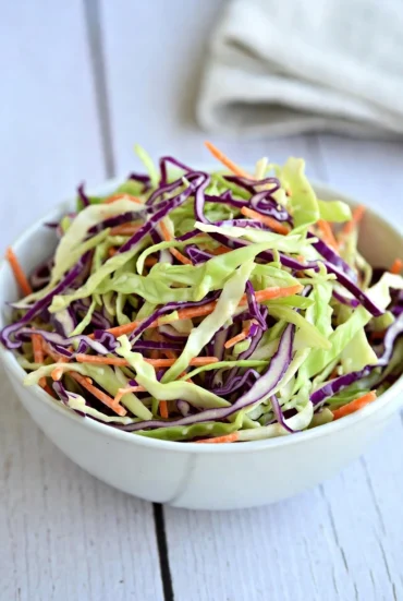 Classic coleslaw served in a white bowl with green cabbage red cabbage and carrots