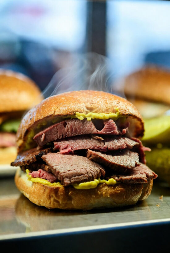 Close-up of a steaming corned beef sandwich stacked with thick slices of beef and yellow mustard on a toasted bun.